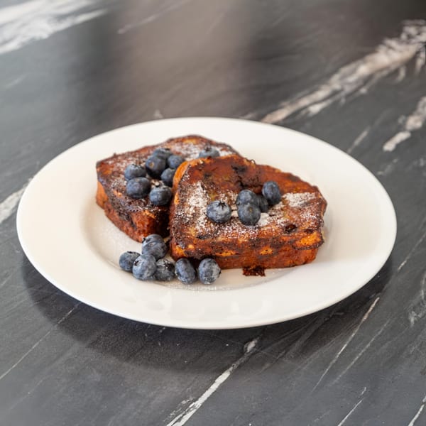 Two slices of Bell the Cat's French toast, topped with blueberries and powdered sugar on a white plate.