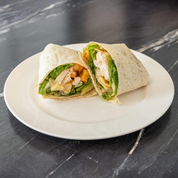 Two halves of a chicken Caesar wrap with lettuce, croutons, and cheese on a white plate.